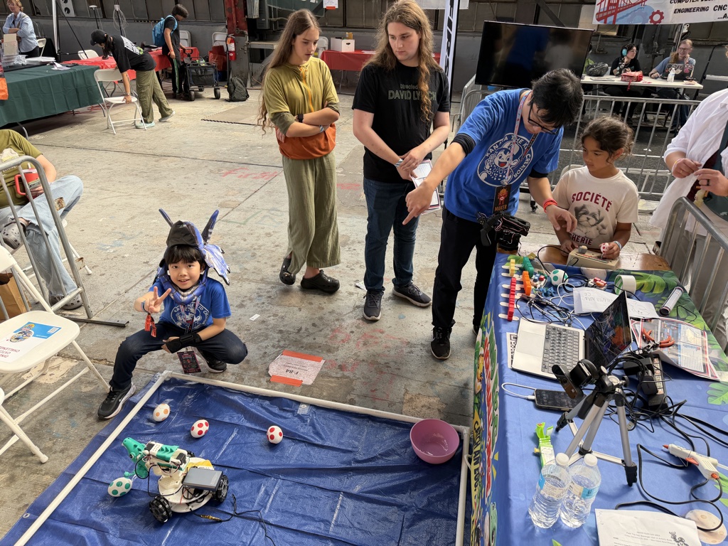 Kanata beside the blue arena while visitors try the dinosaur robot