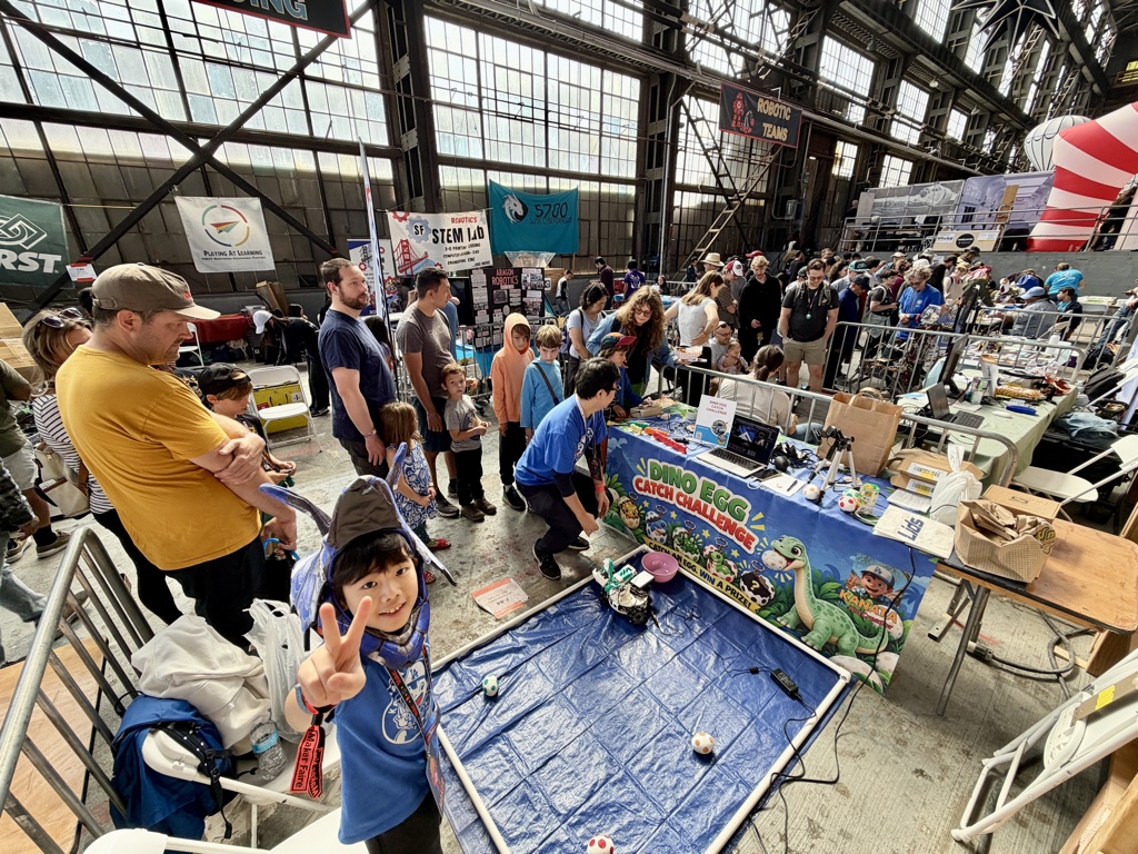 A crowd around the booth inside the Mare Island hall, with Kanata flashing a peace sign