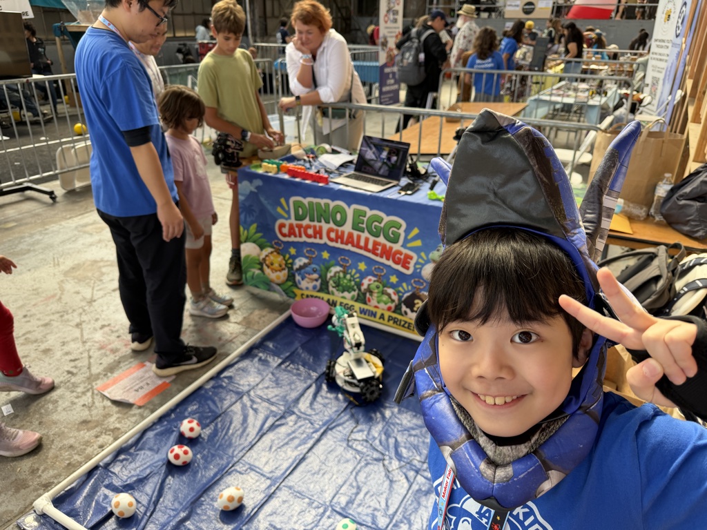 Kanata's selfie in his dinosaur hood with visitors at the booth behind him