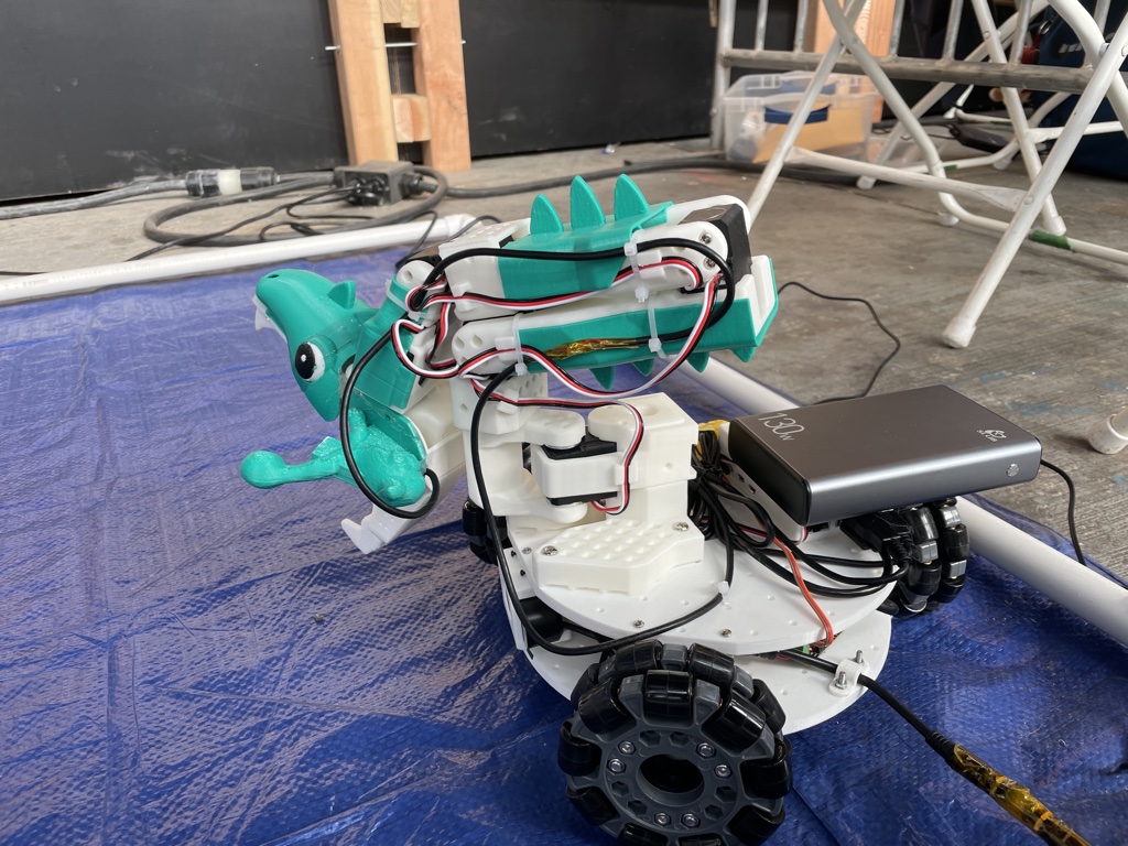 The finished dinosaur robot with its teal 3D-printed head and neck spines on the blue arena